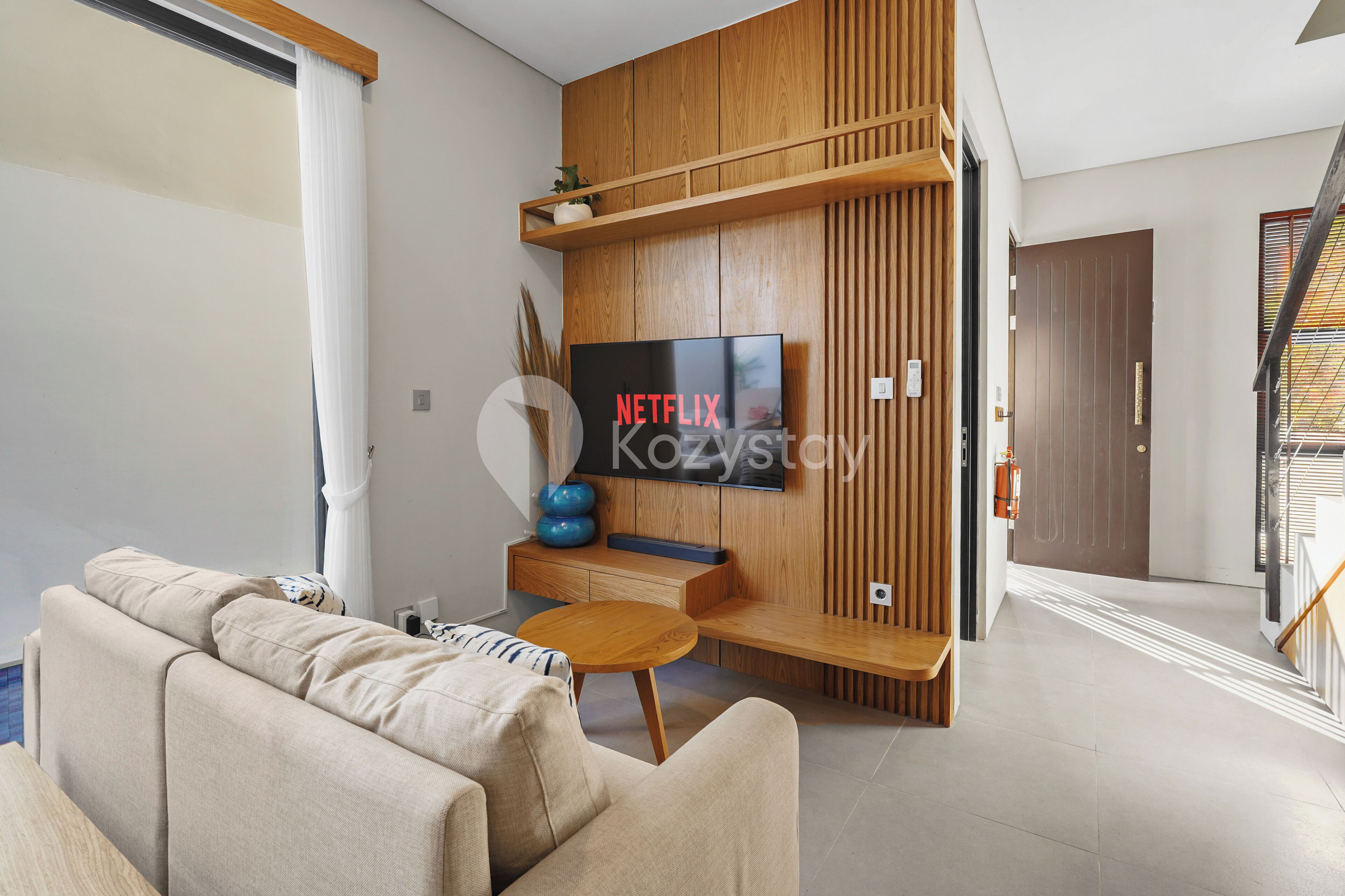 Ein modernes Wohnzimmer mit einem an einer Holzwand montierten Flachbildfernseher, einer Couch, einem Couchtisch und einer Treppe im Hintergrund.
