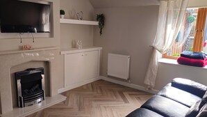 Olohuone, jossa on takka, seinälle asennettu televisio, sohva ja ikkuna, jossa on verhot.