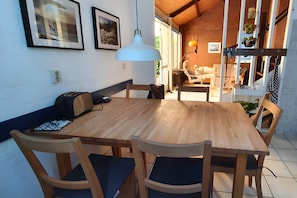 Ein Holztisch mit Stühlen, einer Bank und einer Hängeleuchte in einem Raum mit Holzboden und Blick ins Freie.
