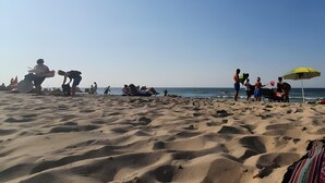 A sandy beach with people, a yellow umbrella, and a boat.