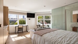 Un dormitorio moderno con una cama grande, un escritorio, una silla y un televisor montado en la pared.