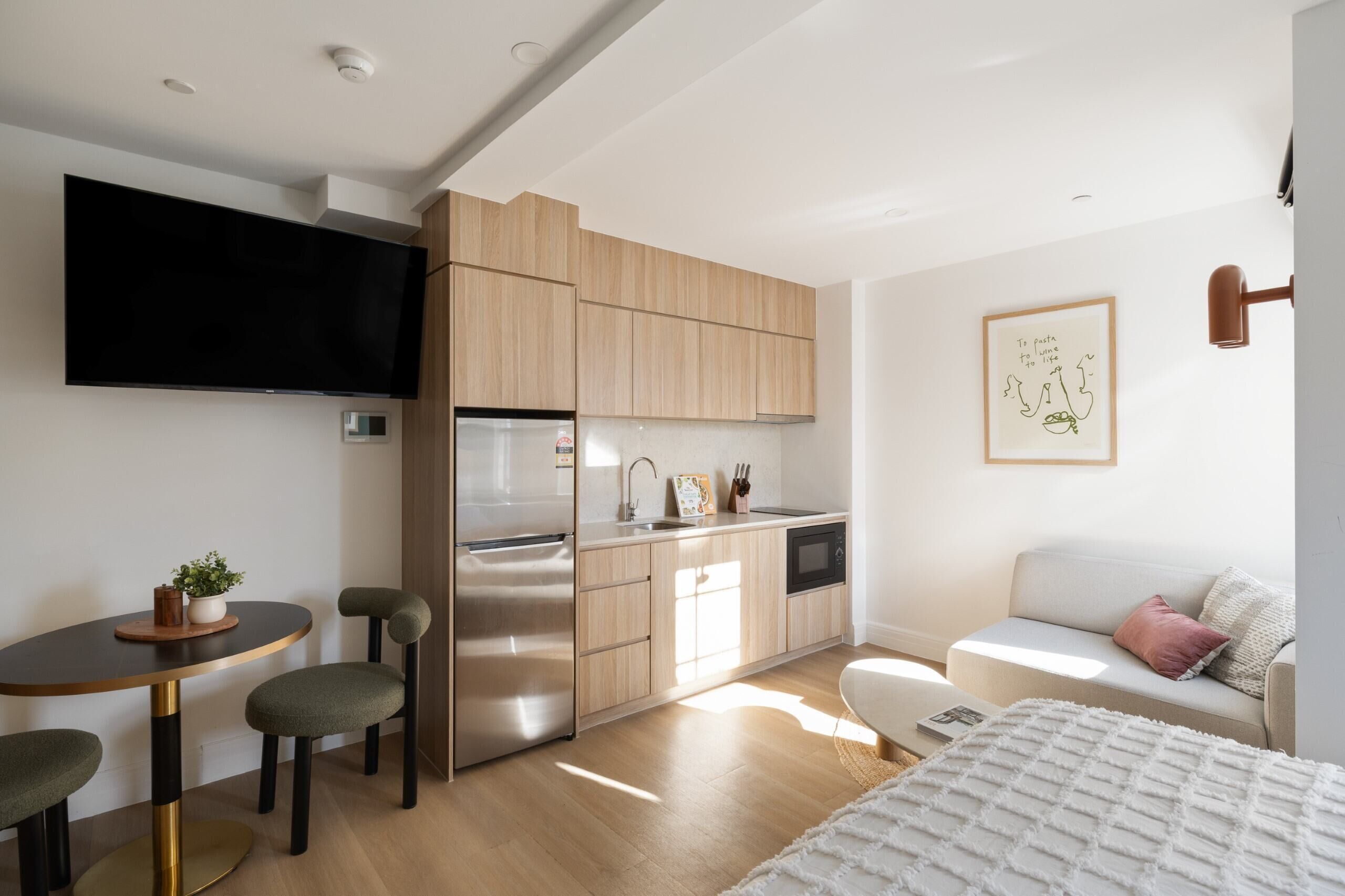 A modern kitchen with a built-in oven, a refrigerator, and a sink. There is a dining table with chairs and a small plant on it.