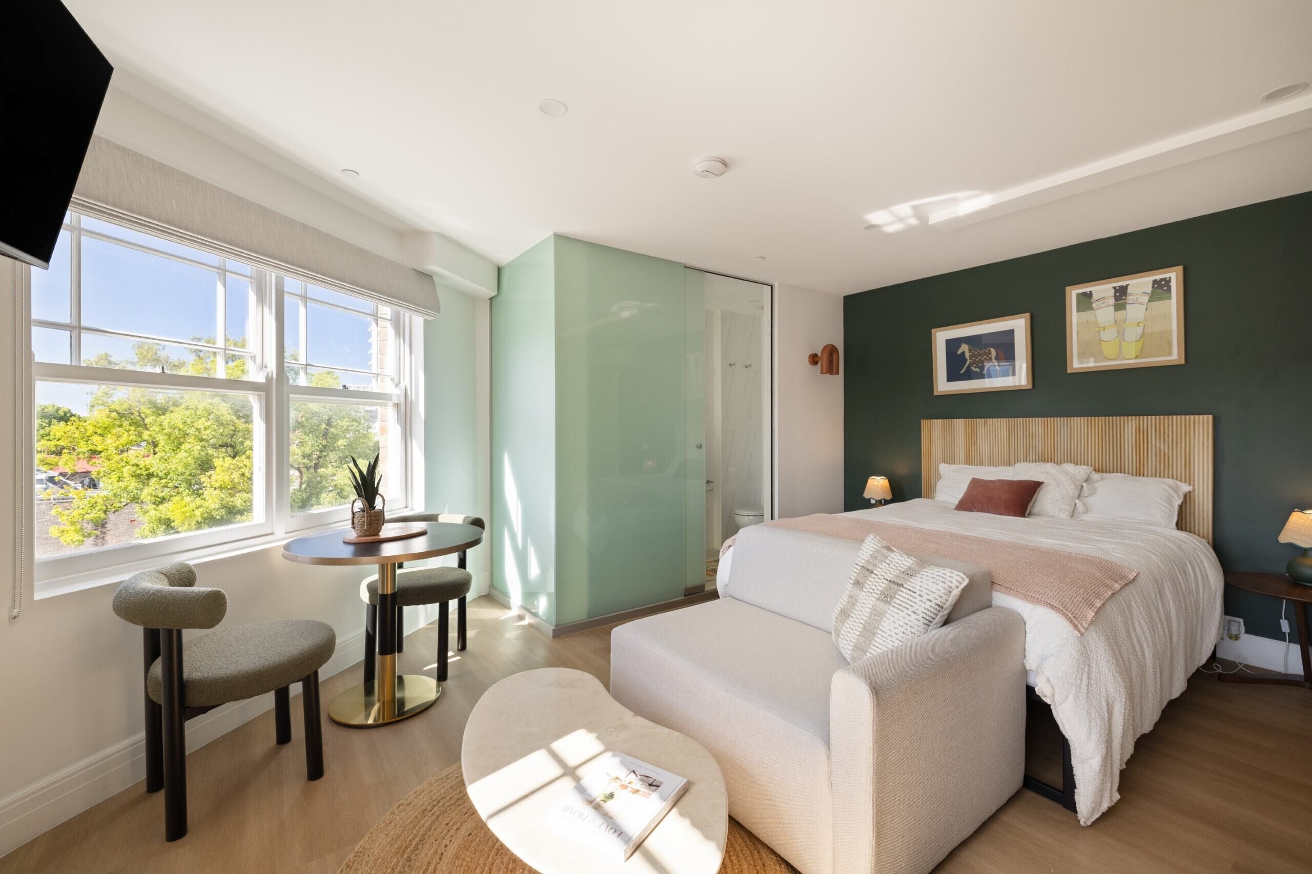 Un dormitorio con cama, escritorio, silla y ventana con vistas a árboles.