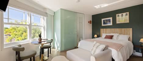 Un dormitorio con cama, escritorio, silla y ventana con vistas a árboles.