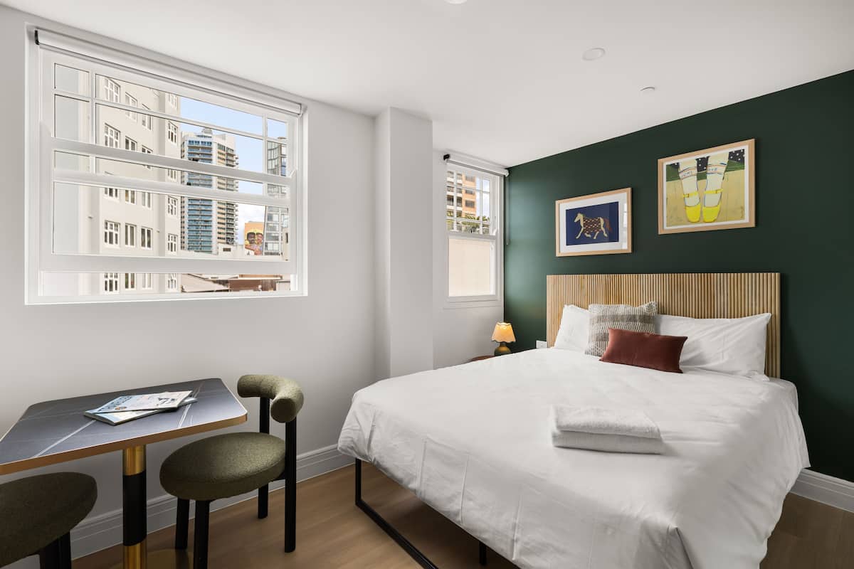 Hotellihuone, jossa on sänky, työpöytä ja ikkuna, josta avautuu näkymä kaupunkiin.