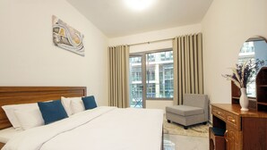 A hotel room with a bed, a desk, a chair, a large window, and a painting on the wall. - Silk Valley-Luxury 1B near Masdar Park (Abu Dhabi)