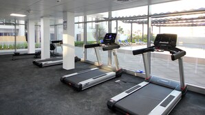 A gym with treadmills, exercise bikes, and a large window with a view of the outdoors. - Silk Valley-Luxury 1B near Masdar Park (Abu Dhabi)
