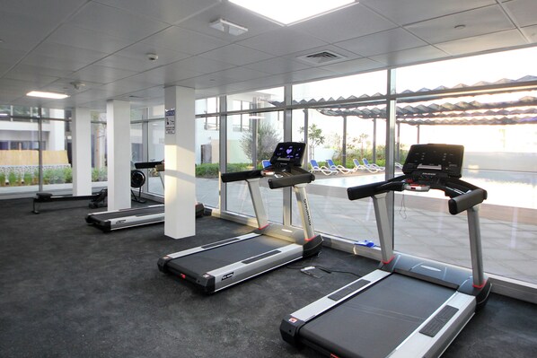 A gym with treadmills, exercise bikes, and a large window with a view of the outdoors. - Silk Valley-Luxury 1B near Masdar Park (Abu Dhabi)