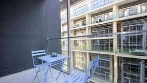 A balcony with a table and chairs, large windows, and a view of a building with multiple floors. - Silk Valley-Luxury 1B near Masdar Park (Abu Dhabi)