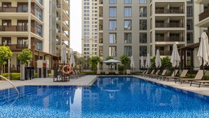 Una piscina rodeada de sillas de descanso y sombrillas, con edificios residenciales altos al fondo.