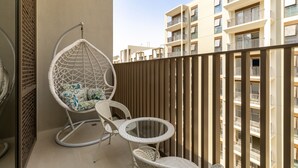 Un balcón con una mecedora, una mesita y vistas a edificios cercanos.