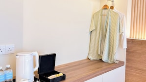 A hotel room with a wooden shelf holding a white kettle, a black box with toiletries, and a robe hanging on a wooden hanger. - Cottonhouz, KK Times Square by Ayuhouz (Kota Kinabalu)