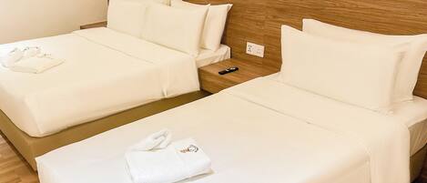 A hotel room with two beds, each with white bedding and pillows, a wooden headboard, and a nightstand with a remote control.