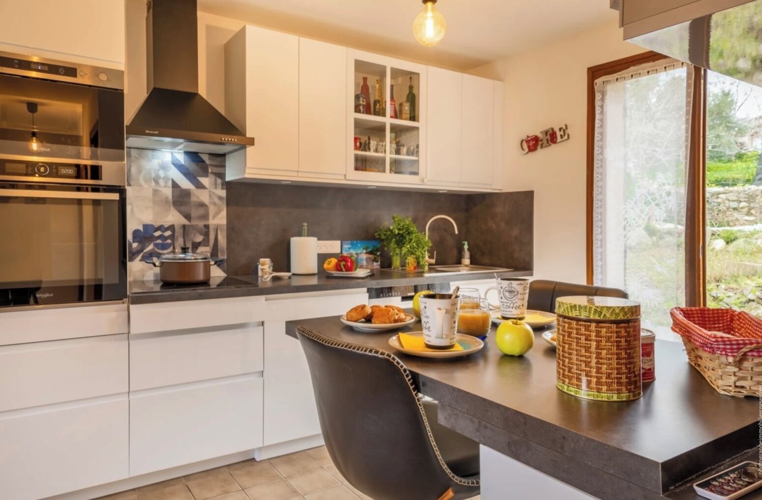 Une cuisine moderne avec des meubles blancs, un plan de travail noir et un coin repas comprenant une chaise et une table.