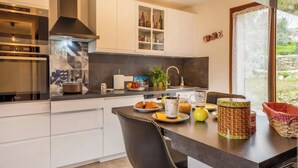 Una cocina moderna con armarios blancos, encimera negra y una zona de comedor con una silla y una mesa.