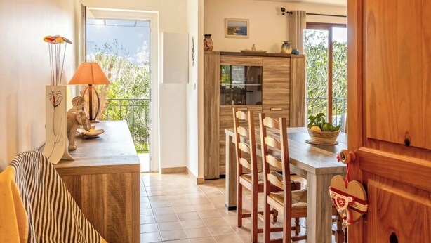 Una cocina moderna con armarios de madera, un comedor con mesa y sillas, y un balcón con vistas a zonas verdes.