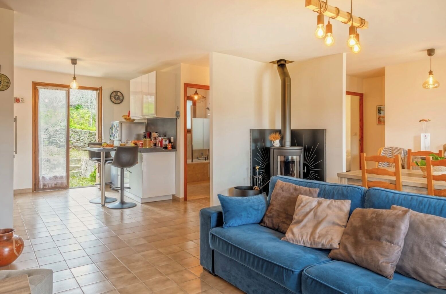 Un salon moderne avec un canapé bleu, un coin cuisine équipé d’une cuisinière et un coin repas avec des chaises en bois.