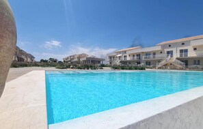 A swimming pool with a clear blue water, surrounded by buildings with balconies and a clear sky.