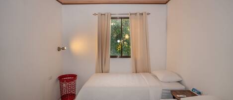 A bedroom with two beds, a window with curtains, a ceiling fan, and a red basket.