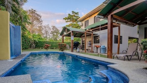Une piscine avec un bord carrelé, un espace de repos couvert et un bâtiment doté d’un toit végétalisé.