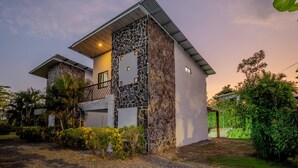 Une maison moderne avec une façade en pierre, un balcon et un jardin bien entretenu.