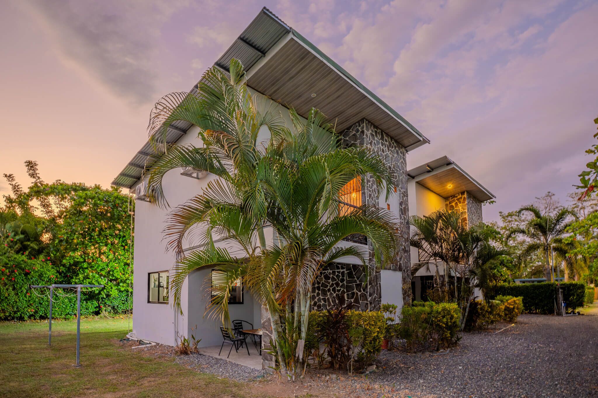 A modern house with a stone facade, a sloped roof, and a garden with palm trees.