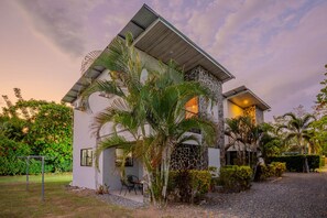 A modern house with a stone facade, a sloped roof, and a garden with palm trees. - Sleep 6-3 bedrooms-1.5 bathrooms-private pool-5 min drive to beach-paved road-easy access (Puntarenas)