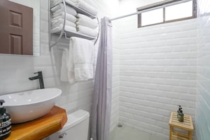 A bathroom with a white sink, a towel rack, a shower curtain, and a small wooden stool.