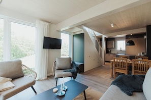 Una sala moderna con sofá, sillón, mesa de comedor y una escalera que conduce a una cocina.