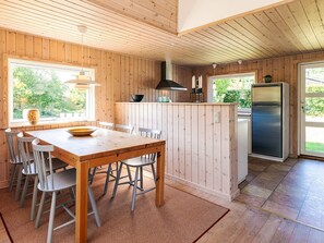 A wooden interior with a dining table, chairs, a kitchen island, a refrigerator, and a window with a view of greenery. - 4 Person Holiday Home in Hals (Hals)