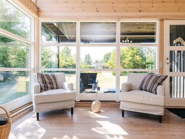 A room with two upholstered chairs, a round table, and a large window with a view of greenery.