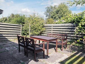 An outdoor seating area with a wooden table and chairs, surrounded by a wooden fence and greenery.