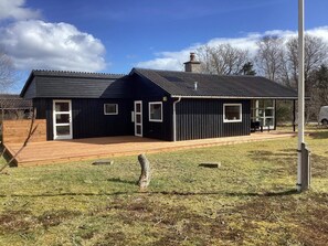 A modern black building with a wooden deck, a chimney, and a covered outdoor seating area.