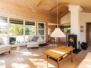 A cozy cabin interior with a wooden ceiling, a fireplace, a dining area, and large windows. - 4 Person Holiday Home in Hals (Hals)