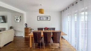 Un espace repas moderne avec une table et des chaises en bois, un luminaire suspendu et un tableau encadré au mur.