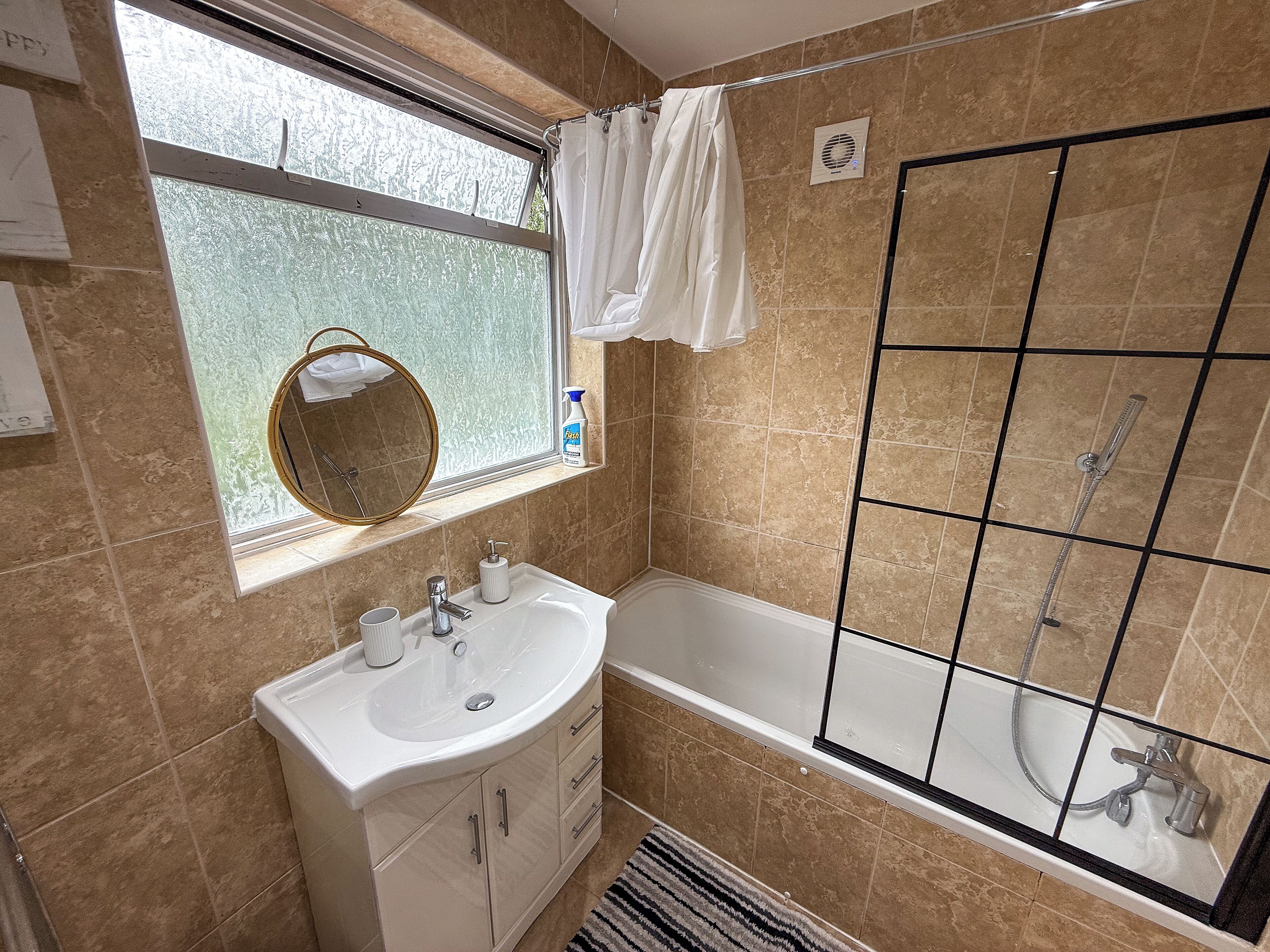 A bathroom with a bathtub, a sink with a mirror, and a window with a view of trees.