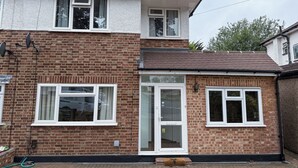 Une maison à deux étages avec une façade en briques, des fenêtres à cadre blanc et une antenne parabolique bien visible.