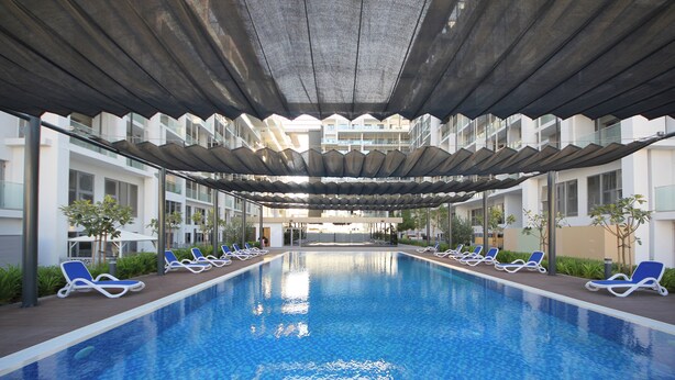 A swimming pool with blue tiled floor, surrounded by lounge chairs and a covered area with a modern architectural design.