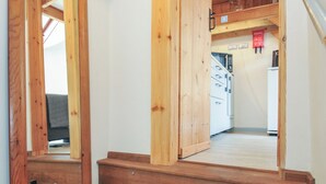 Un escalier en bois mène à un espace cuisine doté de meubles blancs et d’une enseigne rouge accrochée au mur.