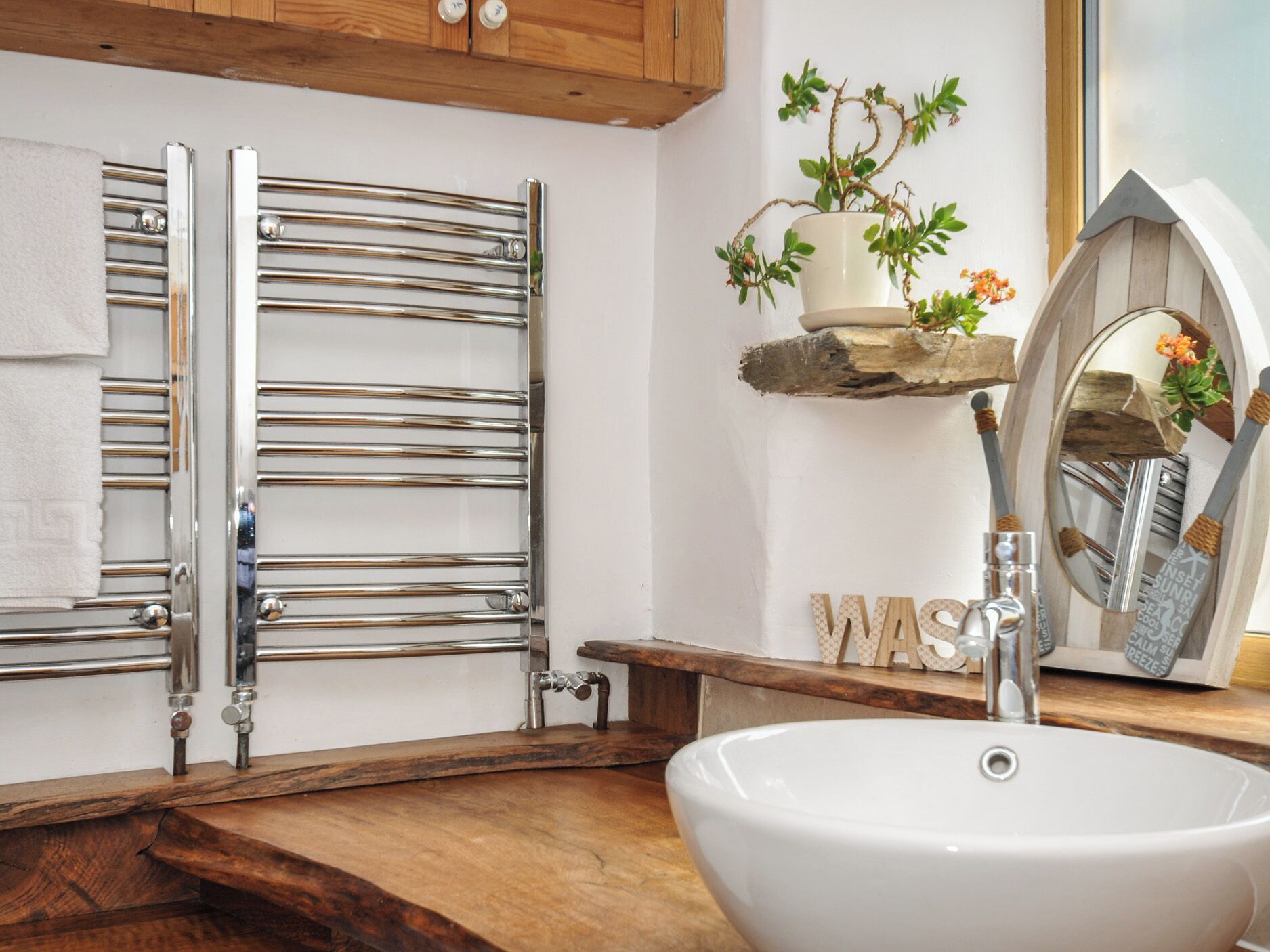 Un baño con lavamanos blanco, toalleros cromados, muebles de madera y un espejo decorativo.