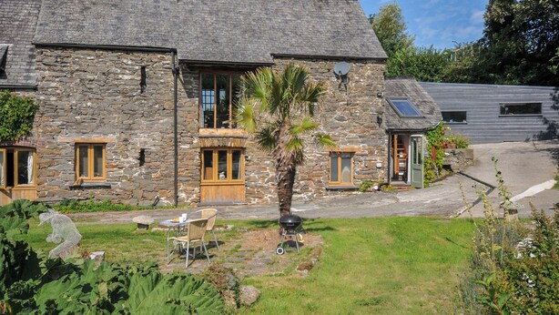 Une petite maison en pierre avec un jardin, une terrasse avec des chaises et une porte bien visible.