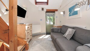 Un salon chaleureux avec un canapé gris, une commode en bois et un téléviseur fixé au mur.