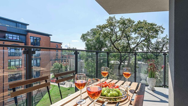 A balcony with a table set for a meal, including wine glasses, a plate of grapes, and a bowl of cherry tomatoes.