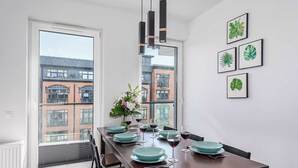 A dining area with a long table set for six, large windows, and framed botanical prints on the wall.