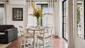 Un coin repas avec une table ronde, des chaises blanches et un vase rempli de fleurs jaunes.