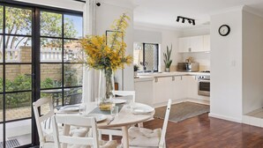 Une cuisine moderne avec des meubles blancs, un coin repas doté d’une table ronde et une grande fenêtre donnant sur l’extérieur.