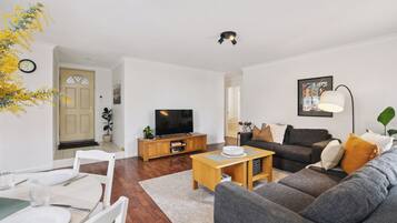 A modern living room with a sofa, coffee table, TV, and dining area.