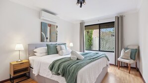 Une chambre à coucher comprenant un lit, des tables de chevet, une chaise, une fenêtre et un appareil de climatisation.