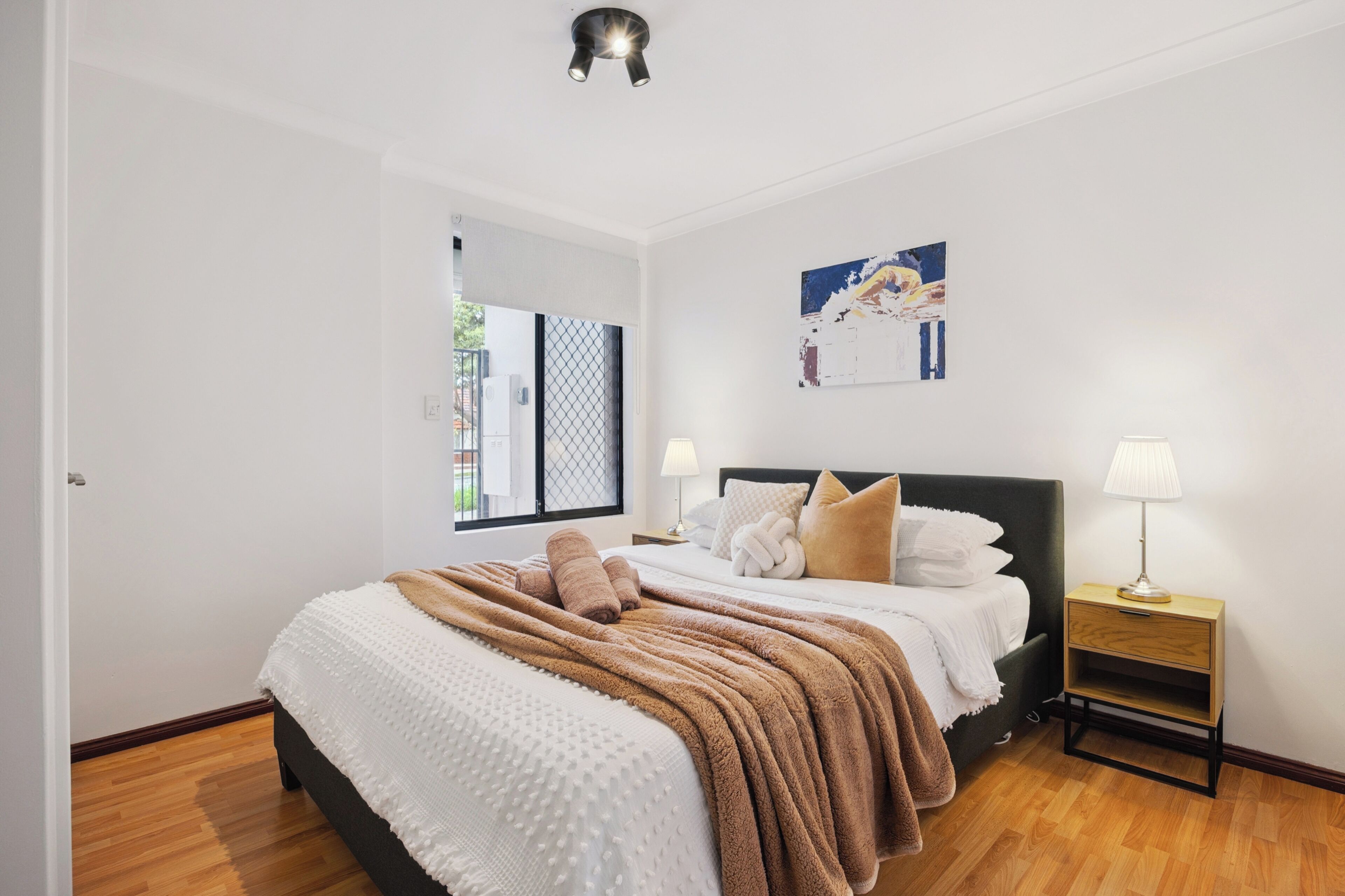 A bedroom with a large bed, two bedside tables, a window with a view, and a wall-mounted artwork.