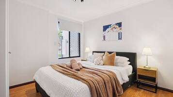 A bedroom with a large bed, two bedside tables, a window with a view, and a wall-mounted artwork.